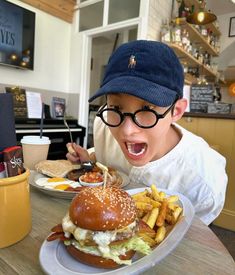 a young boy eating a hamburger and french fries at a fast food restaurant with his mouth wide open