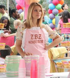 a woman in pink apron standing next to cupcakes