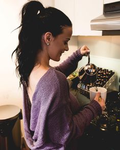 a woman is cooking in the kitchen and she is pouring something into her cup with one hand