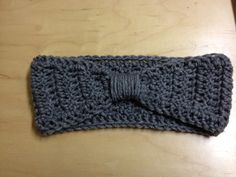 a gray crocheted headband with a bow on the end, sitting on a wooden table