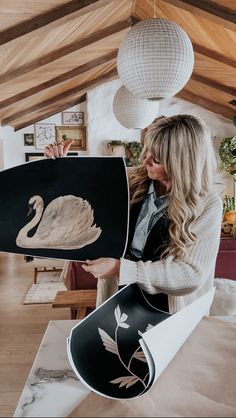 a woman holding up a black and white painting with a swan on it's back