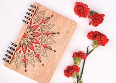 some red carnations are next to a wooden notebook with an intricate design on it