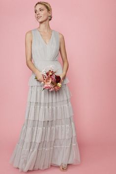 a woman in a long dress holding a bouquet and posing for the camera on a pink background