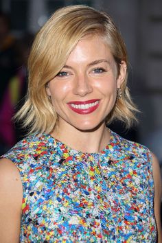 a woman with blonde hair and blue eyes smiles at the camera while wearing a multicolored dress