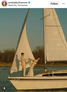 a man and woman on a sailboat in the water with trees in the background