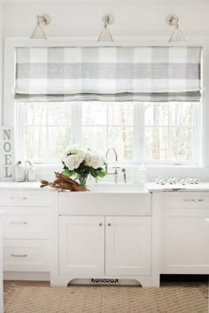 a kitchen with white cabinets and checkered roman shades on the window over the sink