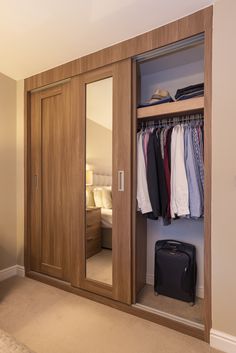 an open closet with clothes hanging on the wall and a suit case sitting in front of it