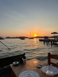 the sun is setting over the water with two plates and glasses on top of it