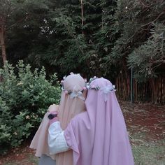 two people dressed up in pink and white robes standing next to each other with trees behind them