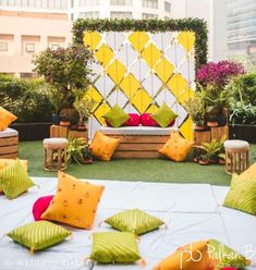 an outdoor seating area with yellow and green pillows on the ground, in front of tall buildings