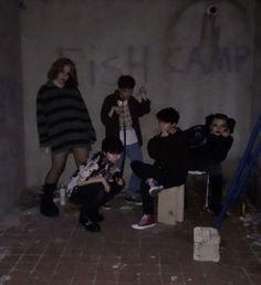 group of young men sitting on stools in an empty room with graffiti written on the wall