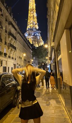 a woman is standing on the sidewalk in front of the eiffel tower at night