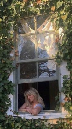 a woman sitting in a window with ivy growing around her and looking out the window