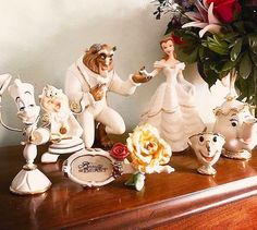 the beauty and the beast figurines are sitting on top of a dresser next to flowers