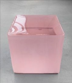 a pink square vase sitting on top of a cement floor next to a white wall