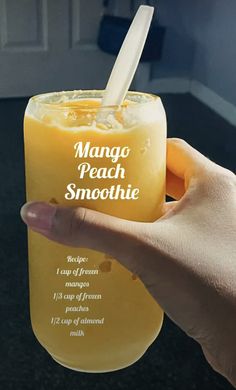 a person holding up a glass with mango peach smoothie in it's hand