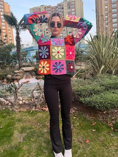 a woman standing in the grass with her hands on her head wearing a colorful sweater