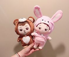 a hand holding two small stuffed animals in pink and brown outfits, one is wearing a bunny costume