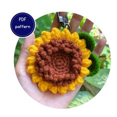 a hand holding a crocheted sunflower keychain in front of a green leafy background