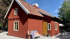 a red house with a white roof and yellow doors on the front, sitting in gravel area next to trees