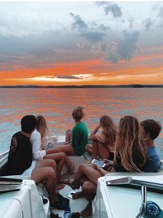 four people sitting on the back of a boat at sunset