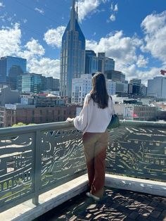 a woman standing on top of a bridge looking at the city