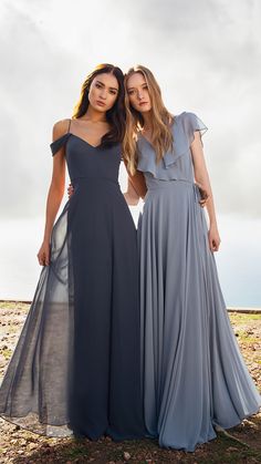 two women standing next to each other in long grey dresses with one wearing a blue dress