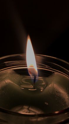 a lit candle in a glass bowl on a dark surface with only one light visible