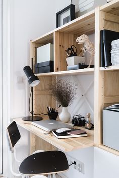 a wooden desk topped with a laptop computer next to a shelf filled with office supplies