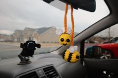 a car dashboard with two stuffed bees hanging from the dash board, and a red car in the background