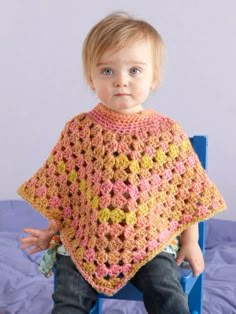 a young child wearing a crocheted ponchy sitting on a blue chair