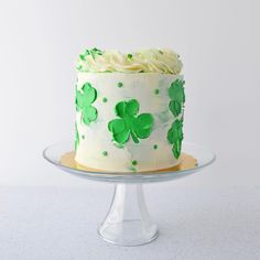 a white cake with green frosting and shamrocks on it sitting on a glass plate