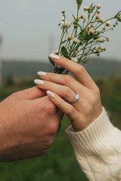 a man and woman holding hands with flowers in front of their faces, both wearing wedding rings