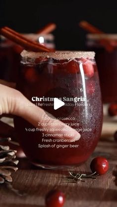 a hand is holding a glass filled with cranberry sangria and cinnamon sticks