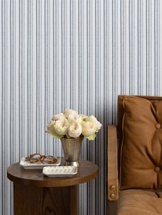 a small table with flowers on it next to a chair and wallpapered walls