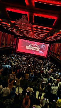 a large group of people in a room with red lighting and a big screen on the ceiling