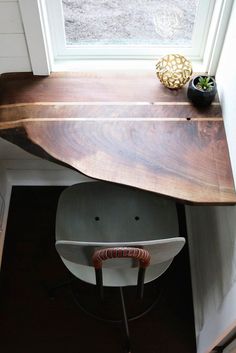 a wooden table sitting under a window next to a white stair case in a house