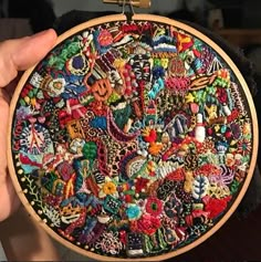 a person holding up a colorful embroidery on a black cloth covered hoop with wooden handles