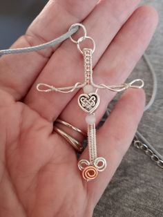 a person holding a silver cross in their hand with two hearts on it and an orange bead