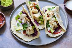 three fish tacos on a plate with avocado and cilantro