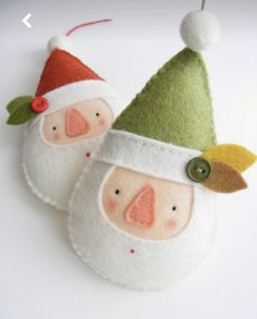 two felt santa claus ornaments hanging on a white table with green and red trimmings