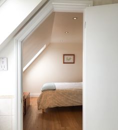 an open door leading to a bedroom with a bed in the corner and wooden floors