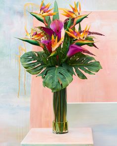 a vase filled with lots of flowers on top of a white table next to a pink wall