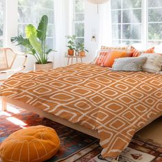 a bed with orange and white comforters in a room next to two large windows