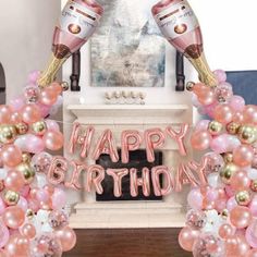 a happy birthday balloon arch with champagne bottles and pink, gold and white balloons in front of a fireplace