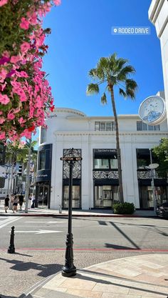 a clock tower on the corner of a street in front of a building with palm trees