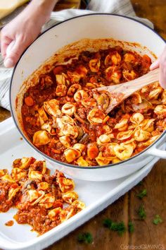 someone is stirring some pasta into a large white pot on a table with other dishes