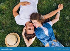 two young people laying on the grass with their arms around each other, looking at the camera