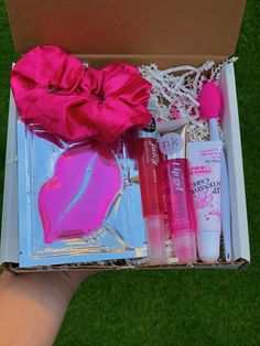 an open box with pink items in it on the green grass and someone's hand