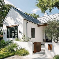 a white house with a metal roof and wooden doors on the front door is surrounded by greenery